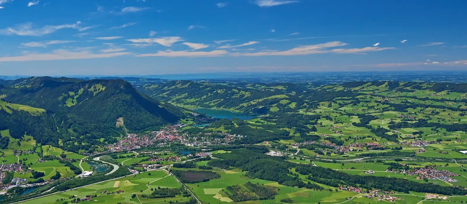 Luftaufnahme von Immenstadt im Allgäu mit Bergen, grünen Wiesen, Flussverlauf und klarer Sicht bis zum Alpsee bei sonnigem Wetter