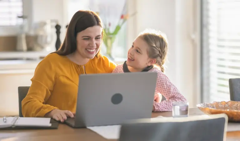 Frau sitzt mit ihrer Tochter am Laptop und arbeitet von zu Hause an der Gründung eines eigenen Onlinehandels