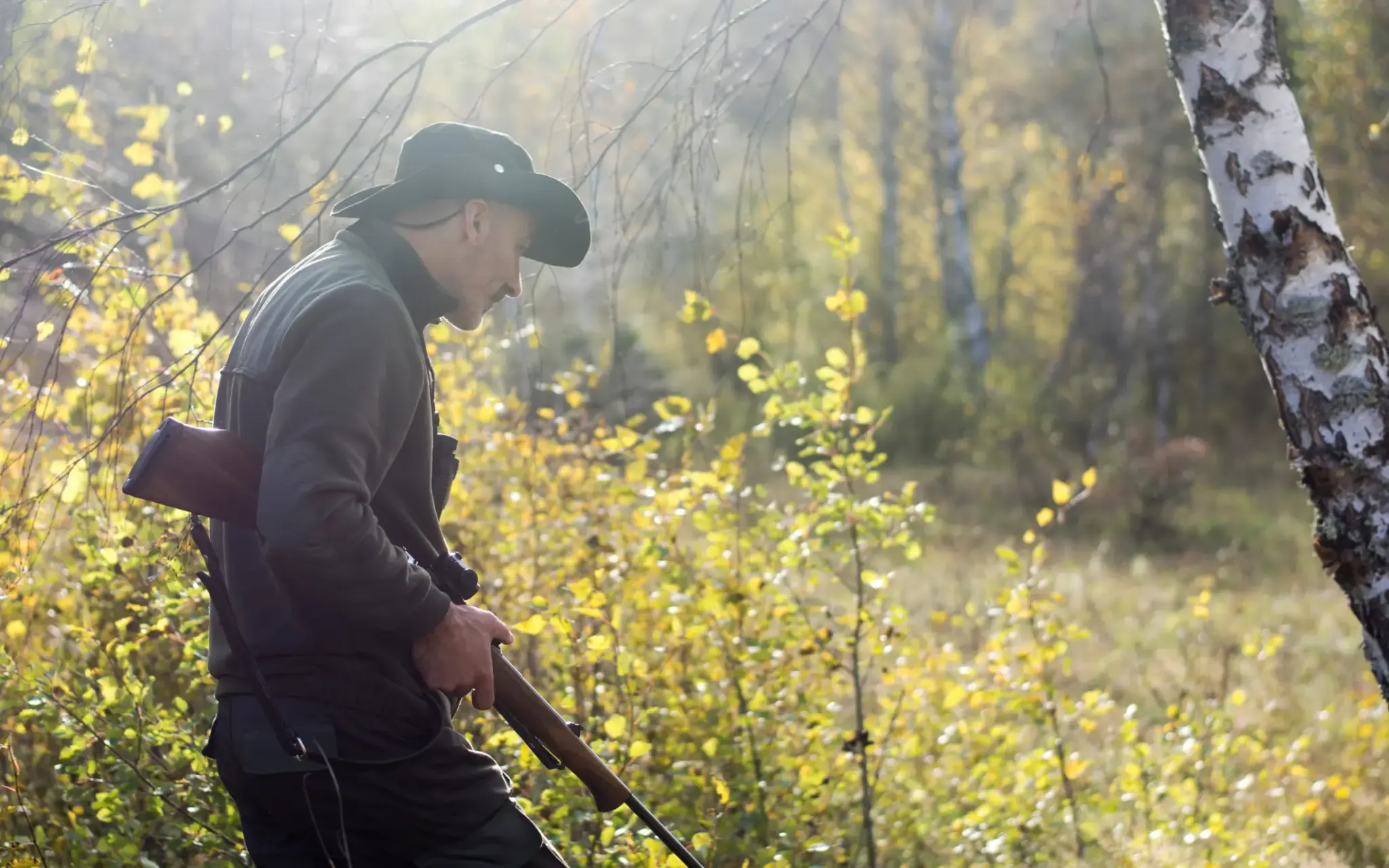 Jäger mit Gewehr im Wald bei Sonnenlicht während eines Streifgangs durch das herbstliche Unterholz