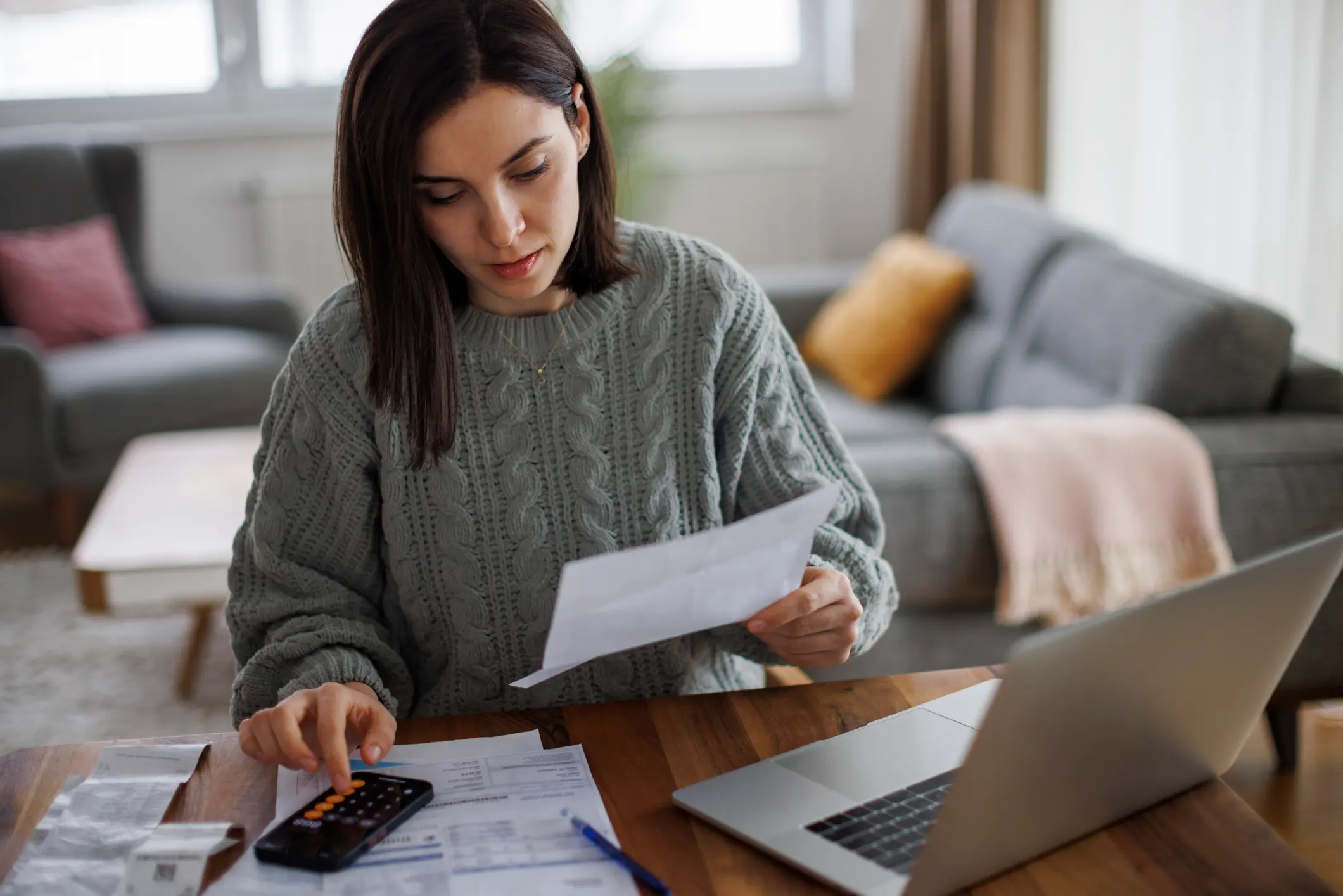 Frau am Tisch mit Laptop, Unterlagen und Smartphone – sie organisiert die Finanzen für ihr Kleingewerbe