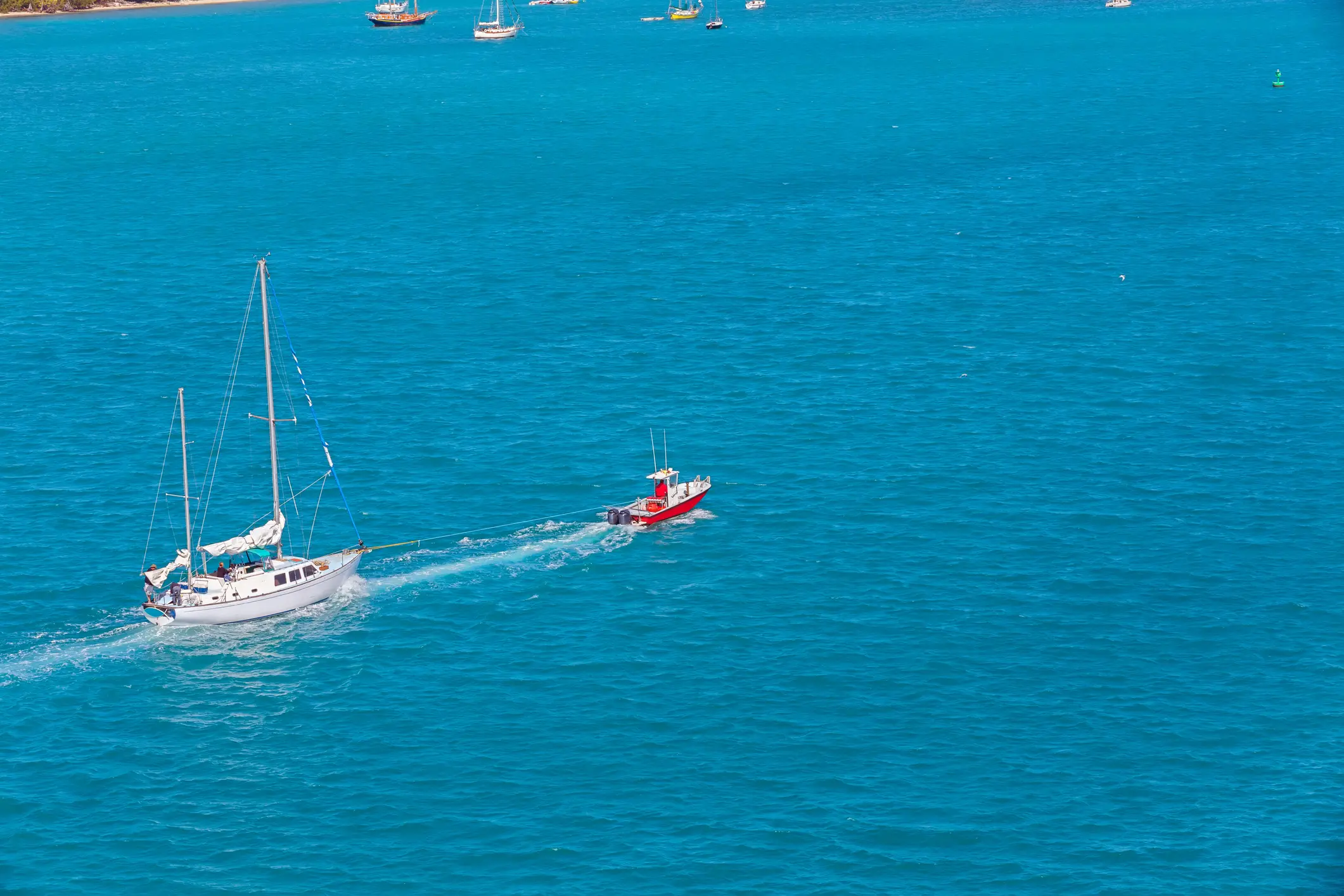 Rotes Motorboot schleppt eine weiße Segelyacht auf offener See – Assistance-Leistungen bei Panne oder Havarie auf dem Wasser