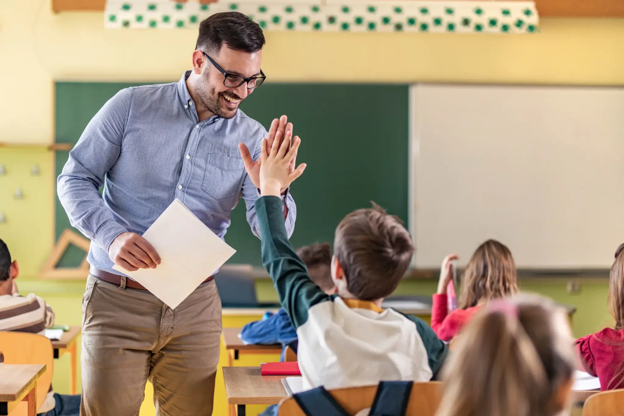 Lehrer im Klassenzimmer gibt einem Schüler ein High-Five – symbolisch für Vertrauen und Verantwortung im Beamtenberuf