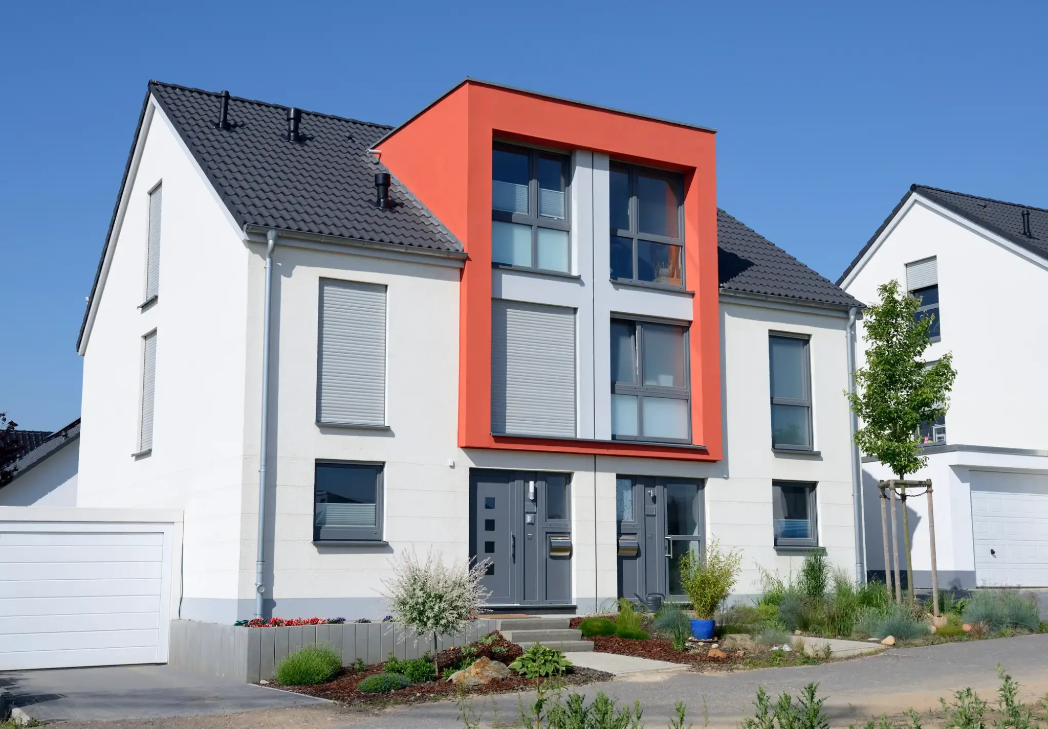 Moderne Doppelhaushälfte mit weißer Fassade, grauem Dach und markantem orangenem Fassadenrahmen