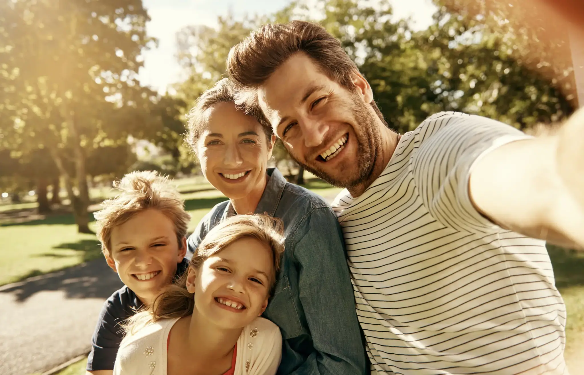 Glückliche Familie mit zwei Kindern macht ein Selfie im Park – Symbolbild für Gesundheit, Vorsorge und Kranken­zusatz­versicherung