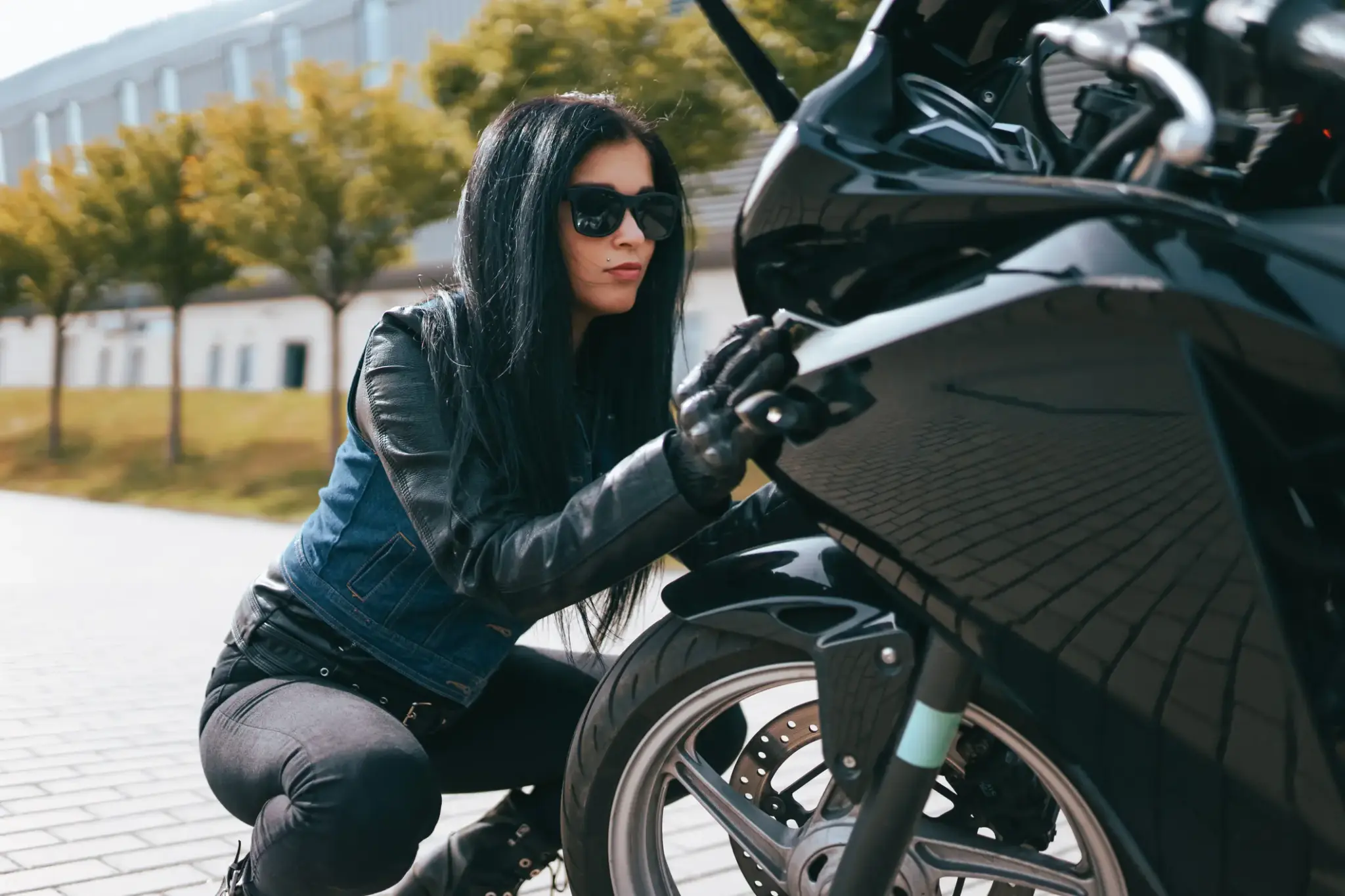 Frau im Lederoutfit prüft ihr Motorrad auf einem Parkplatz – Symbolbild für Motorradversicherung und Sicherheit
