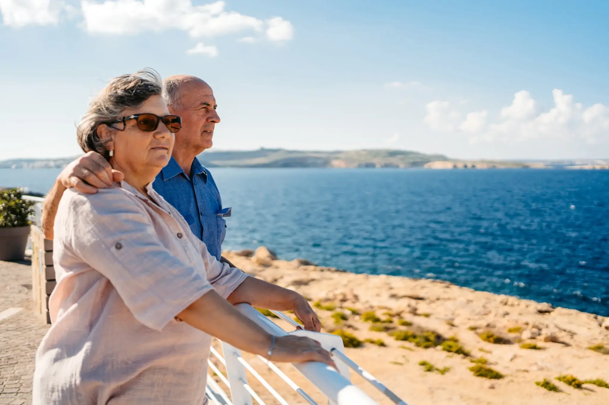 Älteres Paar steht am Meer auf einer Promenade – Symbolbild für Rente im Ausland und Lebensabend in Südeuropa