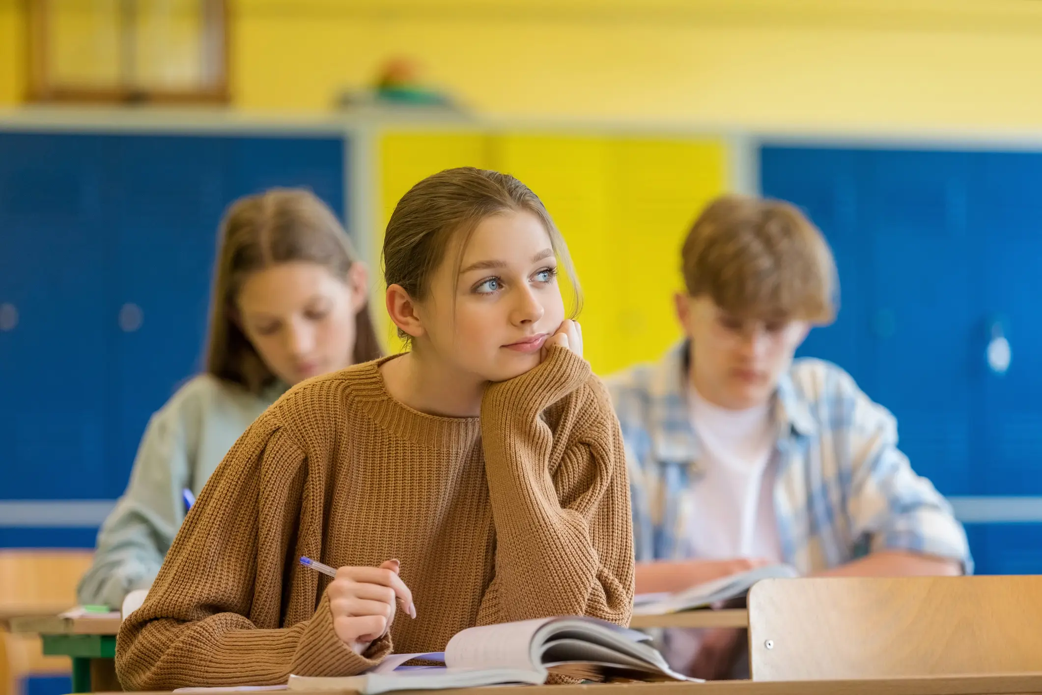 Schülerin denkt verträumt im Klassenzimmer nach, im Hintergrund lernen Mitschüler – Symbol für Zukunft und Absicherung
