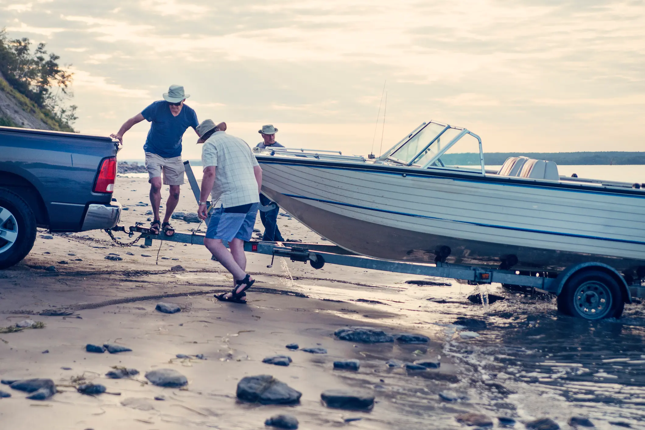 Männer setzen Motorboot mit Trailer am Strand ins Wasser – Absicherung durch Trailer-Versicherung bei Schäden und Transport