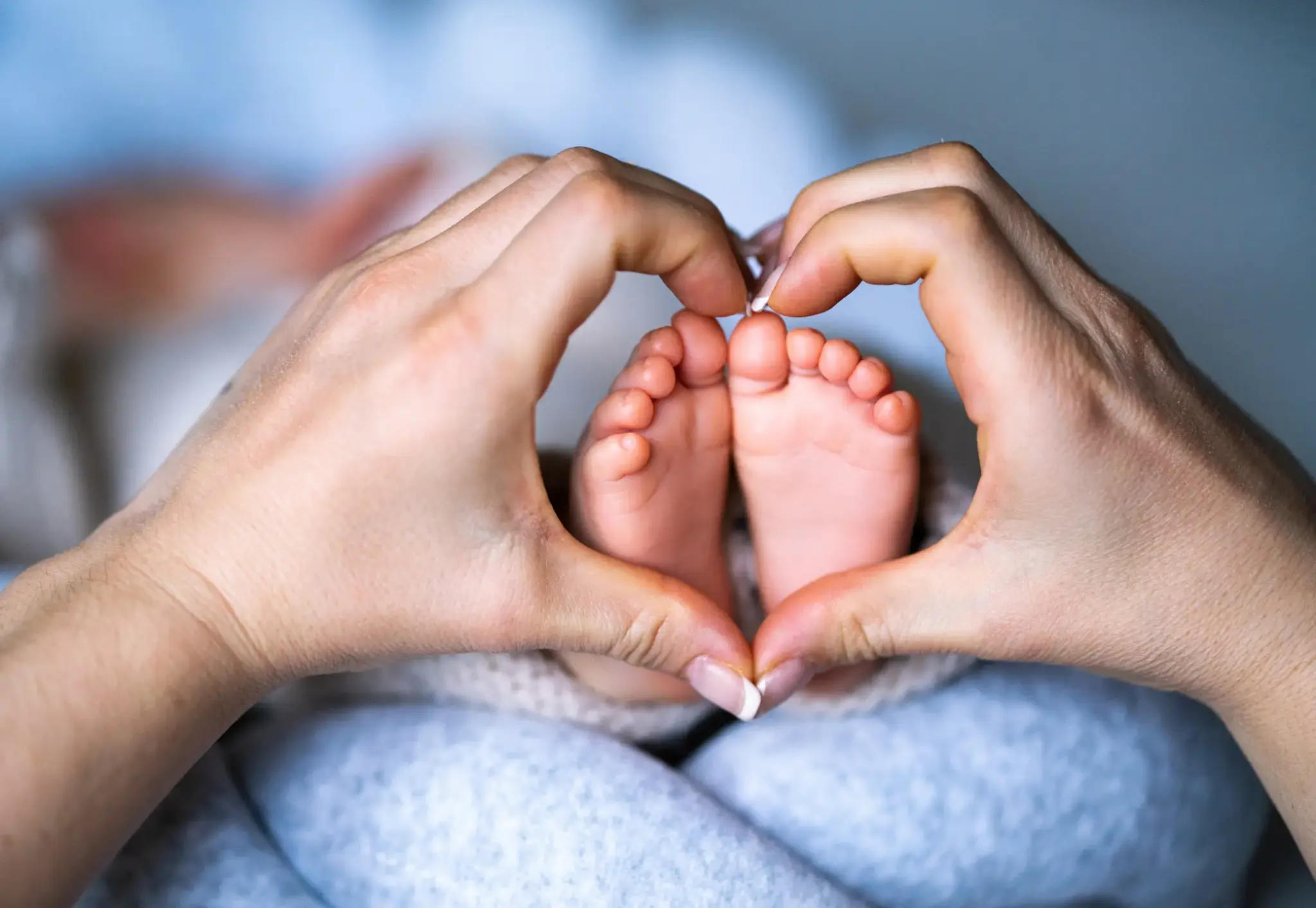 Zwei erwachsene Hände formen ein Herz um die Füße eines Neugeborenen – Symbolbild für Kinderwunsch und künstliche Befruchtung