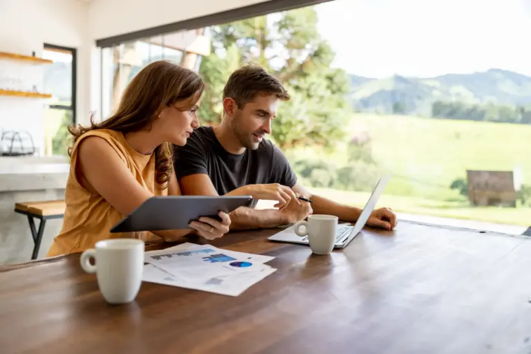 Junges Paar sitzt am Tisch mit Laptop und Unterlagen – Planung und Absicherung im Mietverhältnis durch passende Versicherungen
