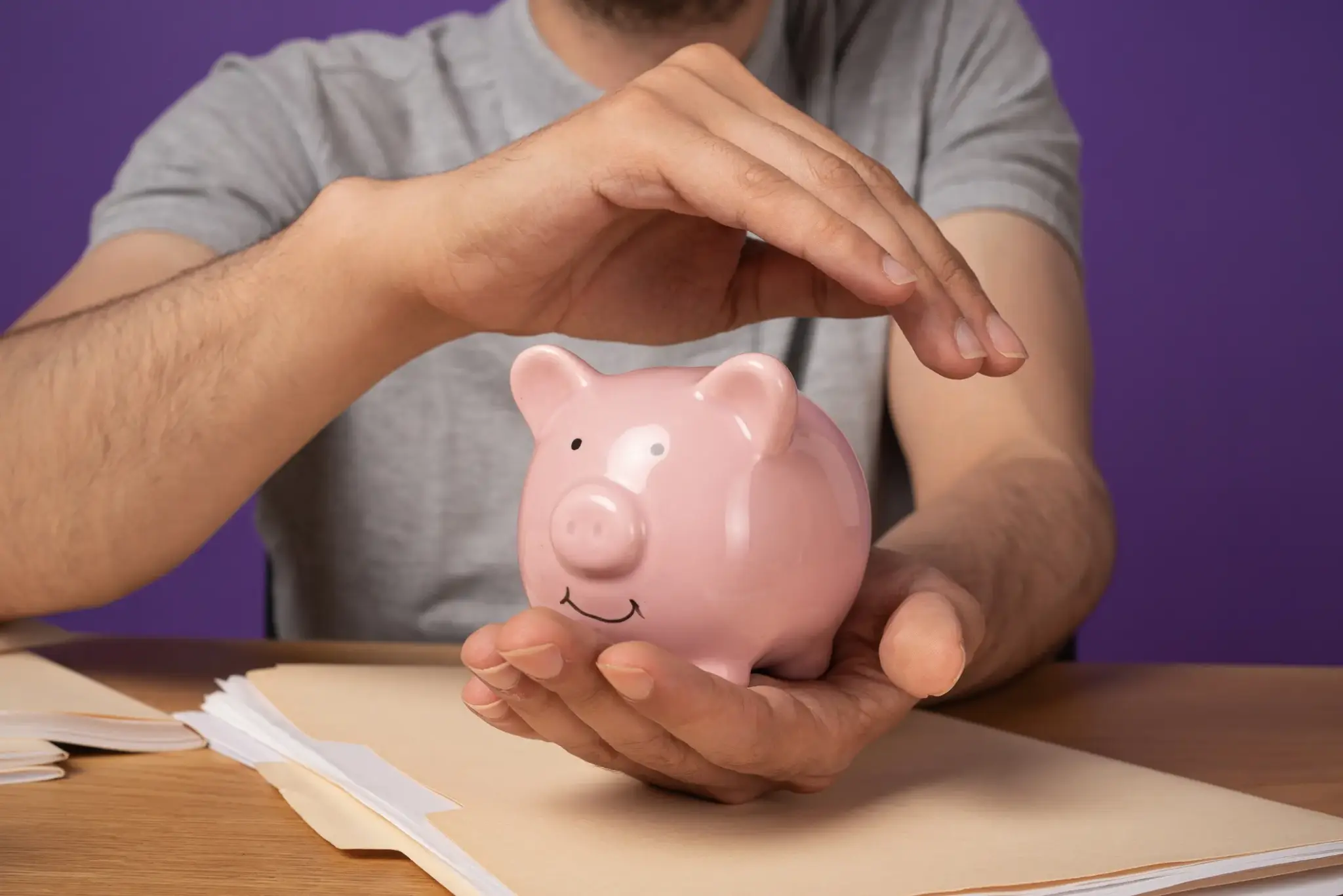 Mann schützt ein rosafarbenes Sparschwein mit seinen Händen – Symbol für finanzielle Sicherheit und kombinierte Vorsorge mit Berufsunfähigkeit.
