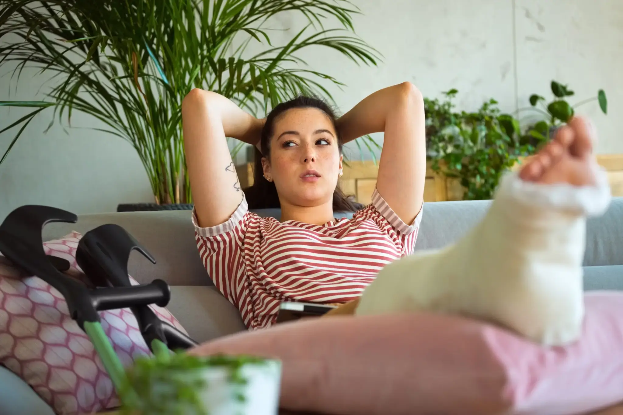 Genesungsgeld | Junge Frau mit Gipsbein liegt auf dem Sofa, Krücken neben ihr – Symbolbild für Verletzung, Auszeit und Anspruch auf Genesungsgeld.