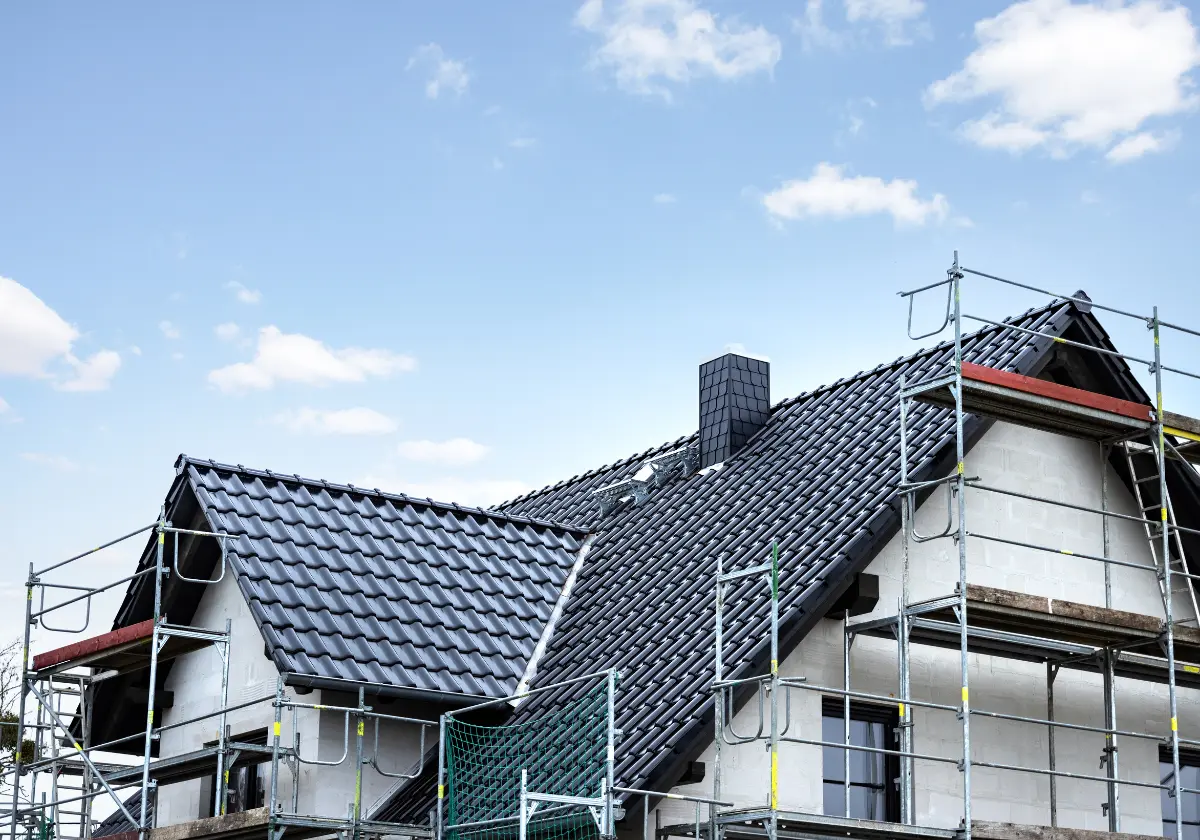 Haus in Bauphase mit neu gedecktem Dach und Baugerüst vor blauem Himmel