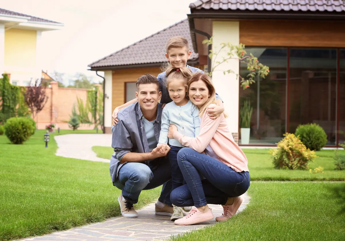Familie sitzt vor Eigenheim mit gelber Fassade und dunklem Walmdach