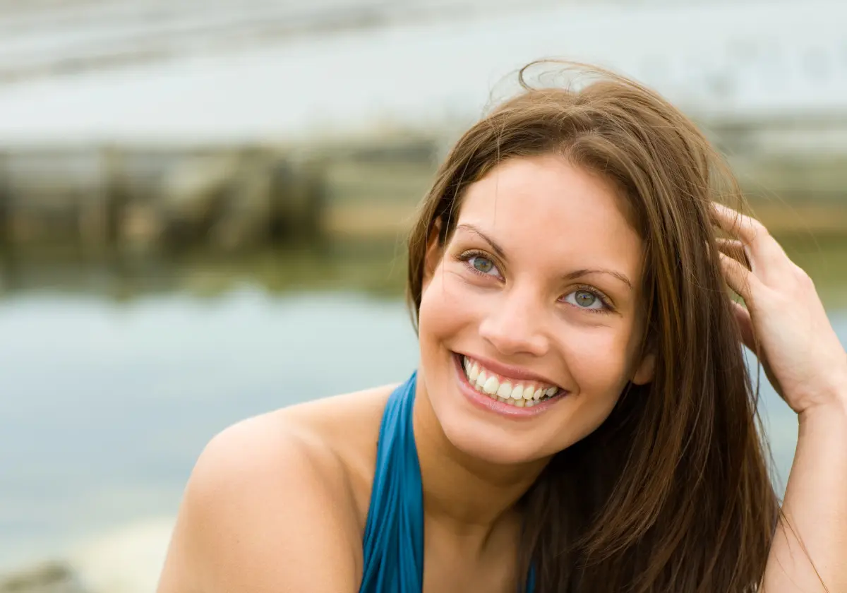 Frau mit langem Haar lacht selbstbewusst in die Kamera vor einem hellen Hintergrund