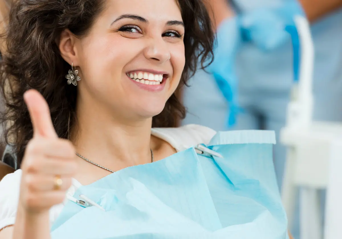 Zufriedene Frau zeigt Daumen hoch nach erfolgreicher Behandlung beim Zahnarzt