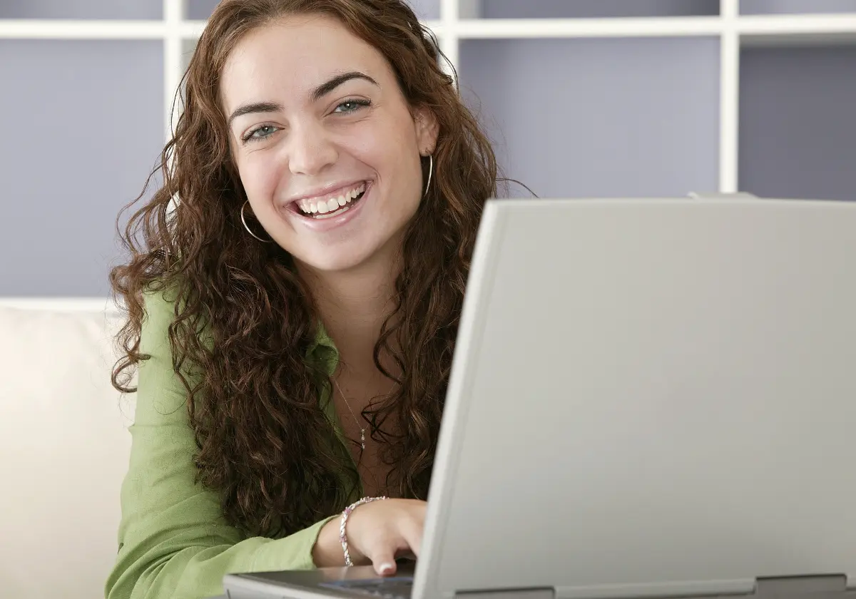 Junge Frau mit lockigen Haaren lächelt am Laptop, sucht Informationen zum Vergleich von Zahnzusatzversicherungen