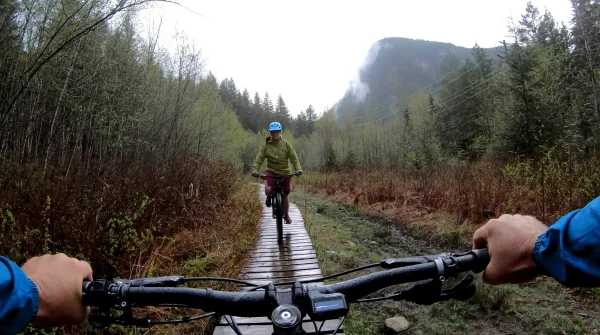 Zwei E-Biker auf nassem Waldweg – Fahrt bei Regen im Gelände mit Akku-Anzeige am Lenker