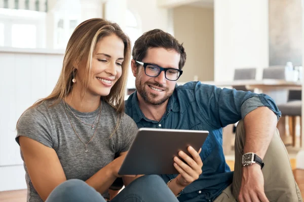 Junges Paar sitzt gemeinsam auf dem Boden und informiert sich digital zur Altersvorsorge auf einem Tablet