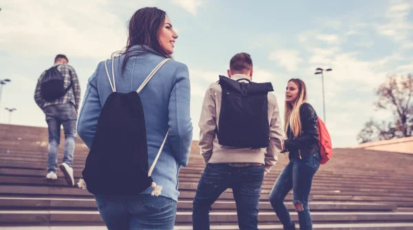 Junge Menschen mit Rucksäcken gehen gemeinsam eine Treppe hoch – symbolisch für Schüler, Studierende und ihren Bildungsweg.