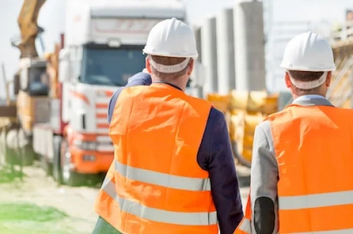 Zwei Bauarbeiter mit Schutzhelmen und Warnwesten auf einer Baustelle – Symbolbild für Versicherungsschutz im Baugewerbe