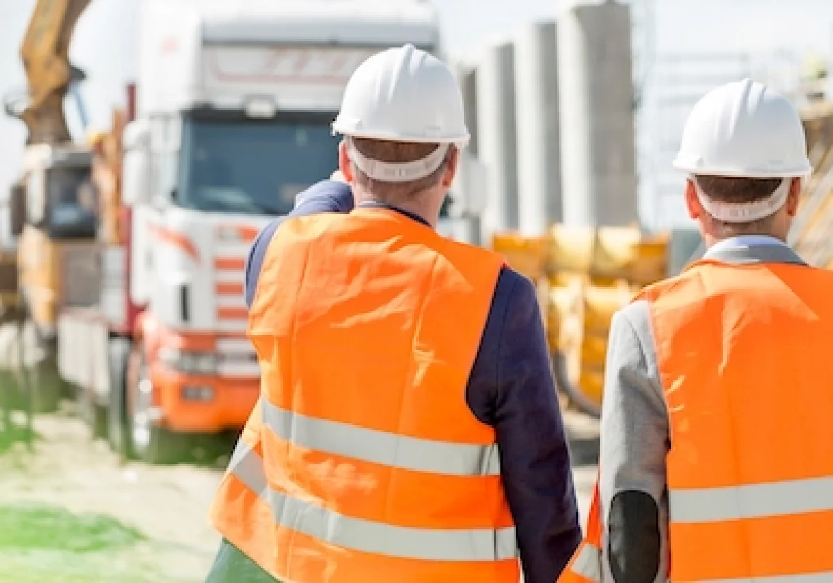 Zwei Bauarbeiter mit Schutzhelmen und Warnwesten auf einer Baustelle – Symbolbild für Versicherungsschutz im Baugewerbe