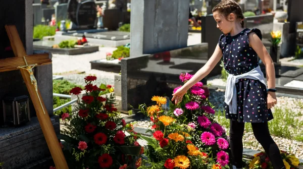Junges Mädchen auf einem Friedhof legt eine Blume auf ein Grab – Symbolbild für Beerdigung, Vorsorge und den Wert frühzeitiger Absicherung.