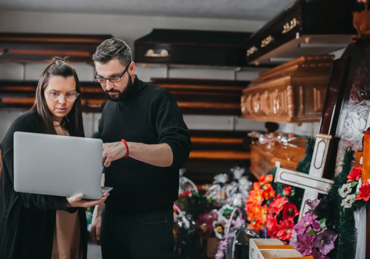 Paar informiert sich am Laptop in einem Bestattungsinstitut über Särge – symbolisch für Planung und Abschluss eines Vorsorgevertrags