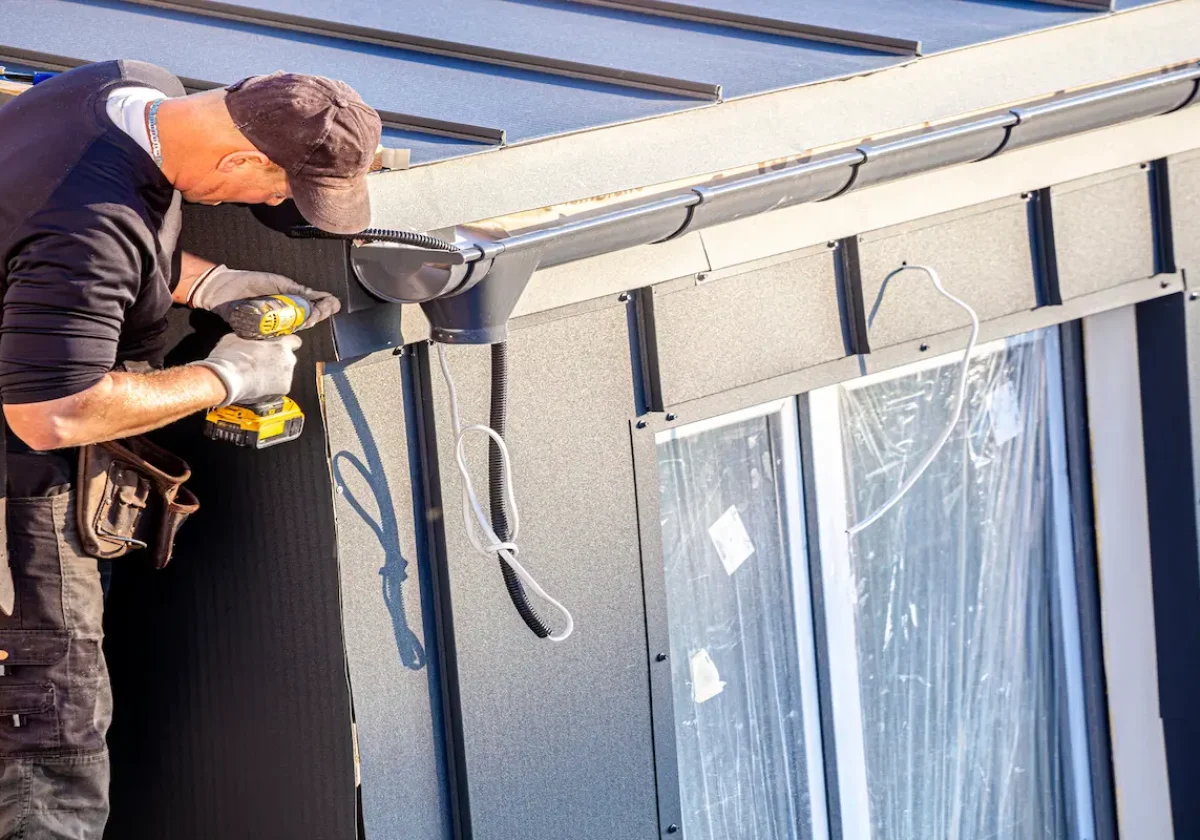 Betriebshaftpflicht Handwerker befestigt Fassadenelemente an einem Neubau mit einem Akkuschrauber bei Sonnenschein
