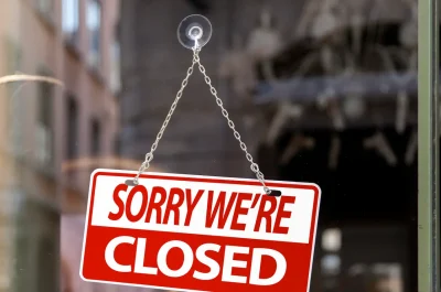 Rotes Hinweisschild mit der Aufschrift „Sorry we’re closed“ an einer Glastür eines Geschäfts