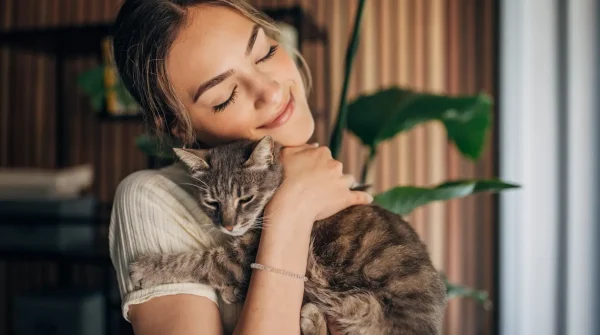 Junge Frau hält liebevoll ihre getigerte Katze im Arm und lächelt – Symbolbild für Sicherheit durch Cleos Katzenkrankenversicherung