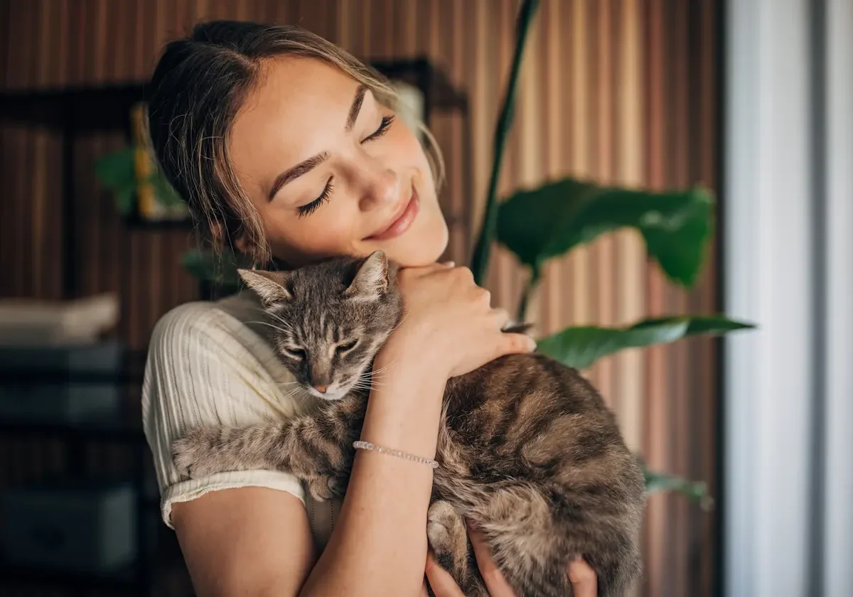 Junge Frau hält liebevoll ihre getigerte Katze im Arm und lächelt – Symbolbild für Sicherheit durch Cleos Katzenkrankenversicherung