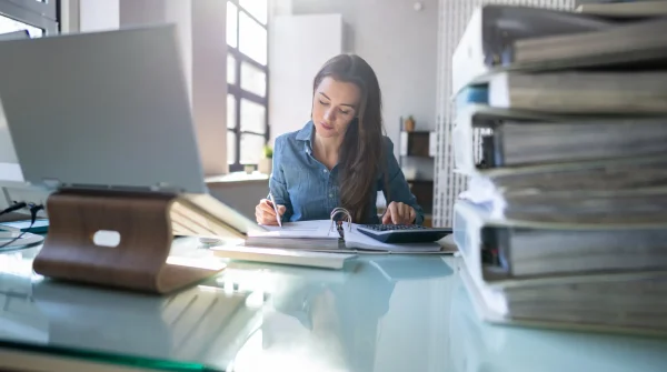 Junge Frau arbeitet konzentriert im Büro mit Akten und Laptop – Symbolbild für Dienstunfähigkeit und Absicherung im Beamtenberuf
