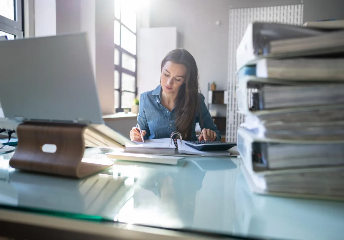 Junge Frau arbeitet konzentriert im Büro mit Akten und Laptop – Symbolbild für Dienstunfähigkeit und Absicherung im Beamtenberuf
