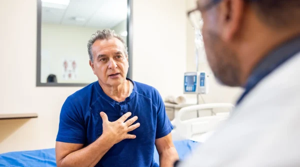 Ein Mann mittleren Alters sitzt auf einem Krankenhausbett und spricht mit einem Arzt – medizinisches Gespräch über eine ernste Diagnose.