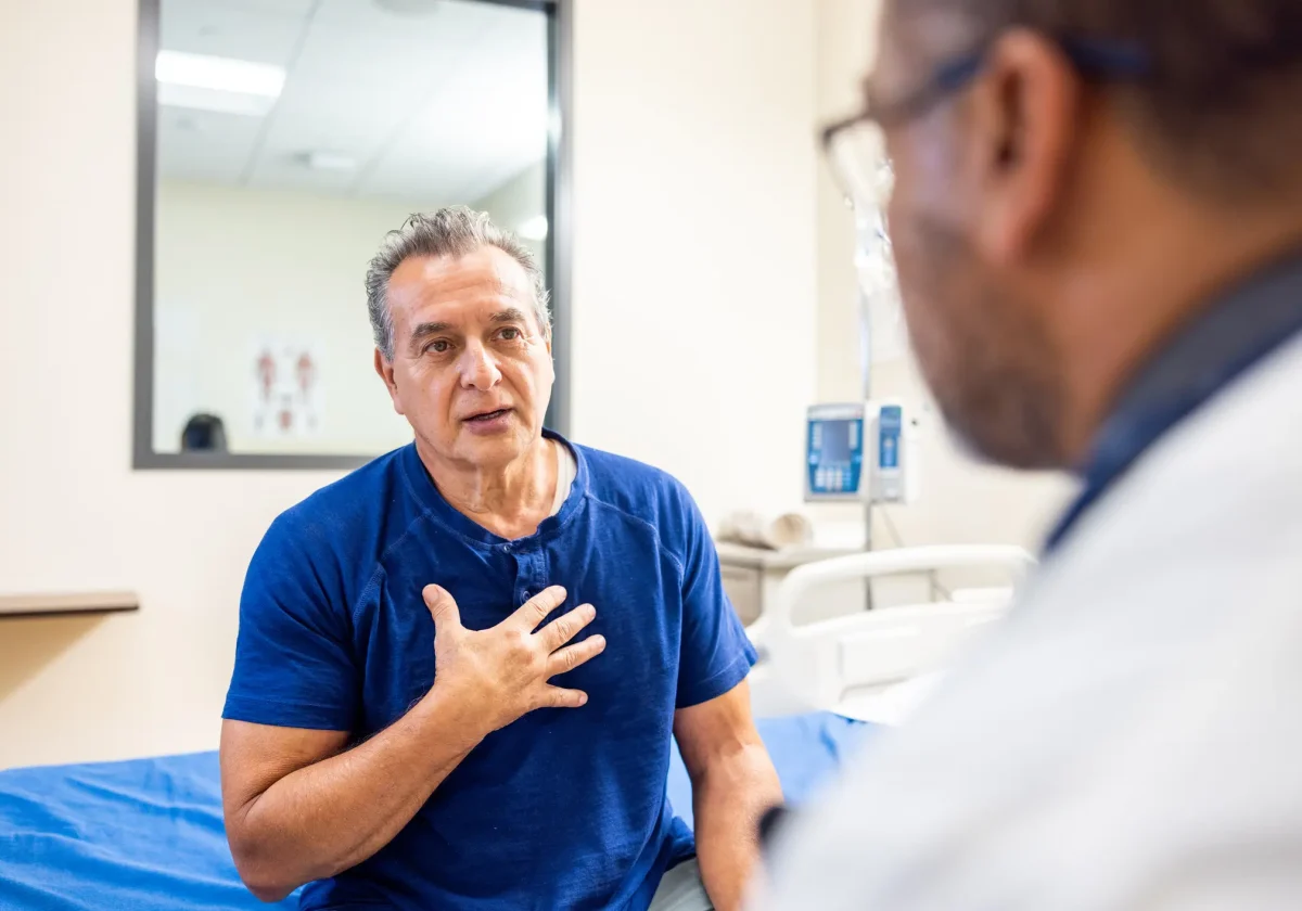 Ein Mann mittleren Alters sitzt auf einem Krankenhausbett und spricht mit einem Arzt – medizinisches Gespräch über eine ernste Diagnose.