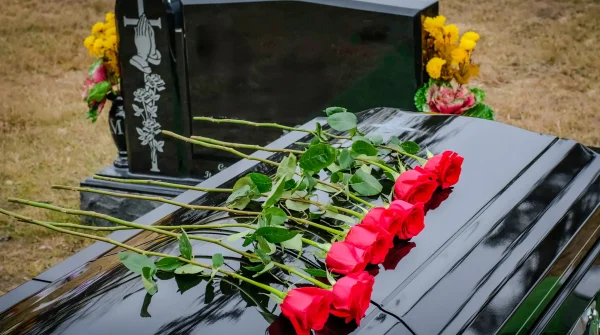 Mehrere rote Rosen liegen auf einem glänzenden schwarzen Sarg vor einem Grabstein – symbolisches Bild für eine traditionelle Erdbestattung