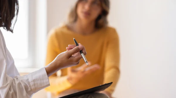 Frau im Gespräch mit Fachperson, Fokus auf Stift und Notizen – symbolisiert Beratung zu Krankheiten als Ursache für Erwerbsminderungsrente