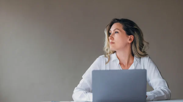 Nachdenkliche Frau sitzt mit Laptop am Tisch und blickt zur Seite – symbolisiert Unsicherheit und Fragen zur Erwerbsminderungsrente