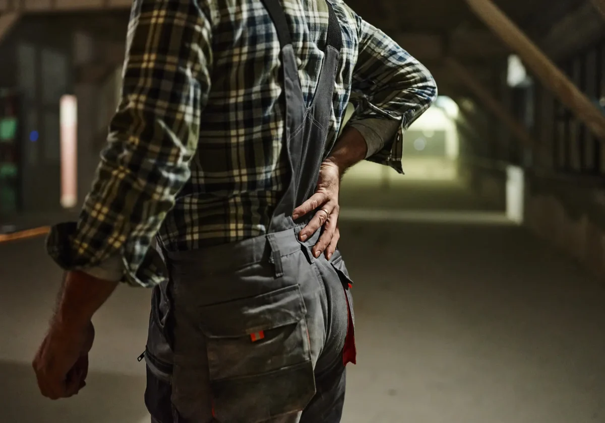 Arbeiter in Latzhose fasst sich an den schmerzenden Rücken – symbolisiert körperliche Belastung und mögliche Erwerbsunfähigkeit im Beruf