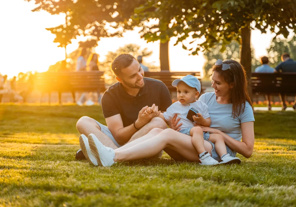 Junge Familie sitzt gemeinsam im Park auf der Wiese und genießt den Moment – Symbolbild für Sicherheit und Lebensqualität durch Absicherung.