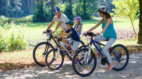 Familie mit zwei Kindern fährt gemeinsam Fahrrad im Wald – Familienzeit mit Schutzhelm und Bewegung an der frischen Luft