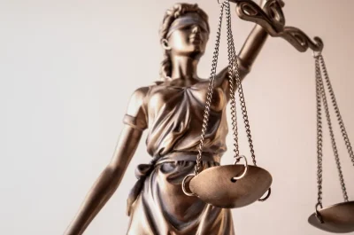 Firmen-Rechtsschutz Bronzefarbene Justitia-Figur mit Waage und verbundenen Augen vor hellem Hintergrund – Symbol für Gerechtigkeit im Rechtswesen