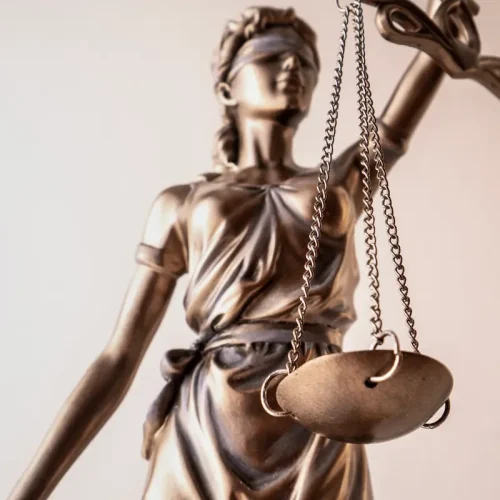 Bronzefarbene Justitia-Figur mit Waage und verbundenen Augen vor hellem Hintergrund – Symbol für Gerechtigkeit im Rechtswesen