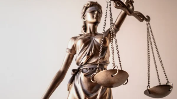 Bronzefarbene Justitia-Figur mit Waage und verbundenen Augen vor hellem Hintergrund – Symbol für Gerechtigkeit im Rechtswesen