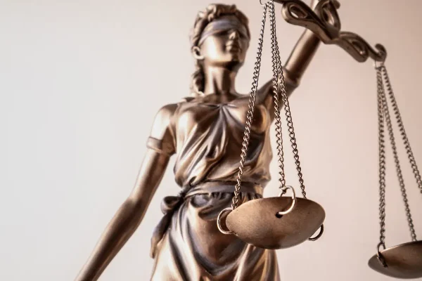 Bronzefarbene Justitia-Figur mit Waage und verbundenen Augen vor hellem Hintergrund – Symbol für Gerechtigkeit im Rechtswesen