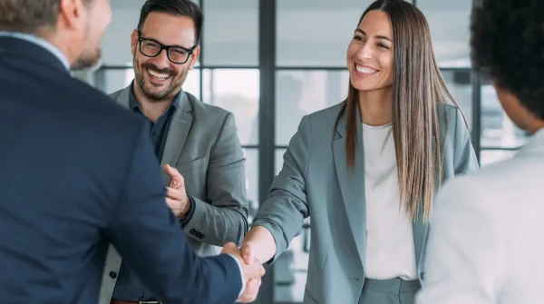 Geschäftsleute begrüßen sich mit einem Handschlag in einem modernen Büro mit Glasfront im Hintergrund