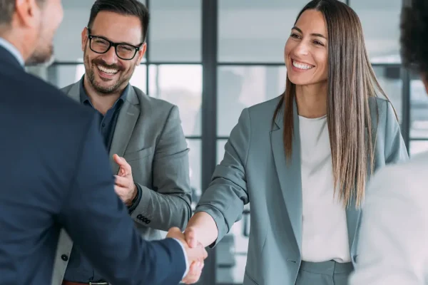 Geschäftsleute begrüßen sich mit einem Handschlag in einem modernen Büro mit Glasfront im Hintergrund
