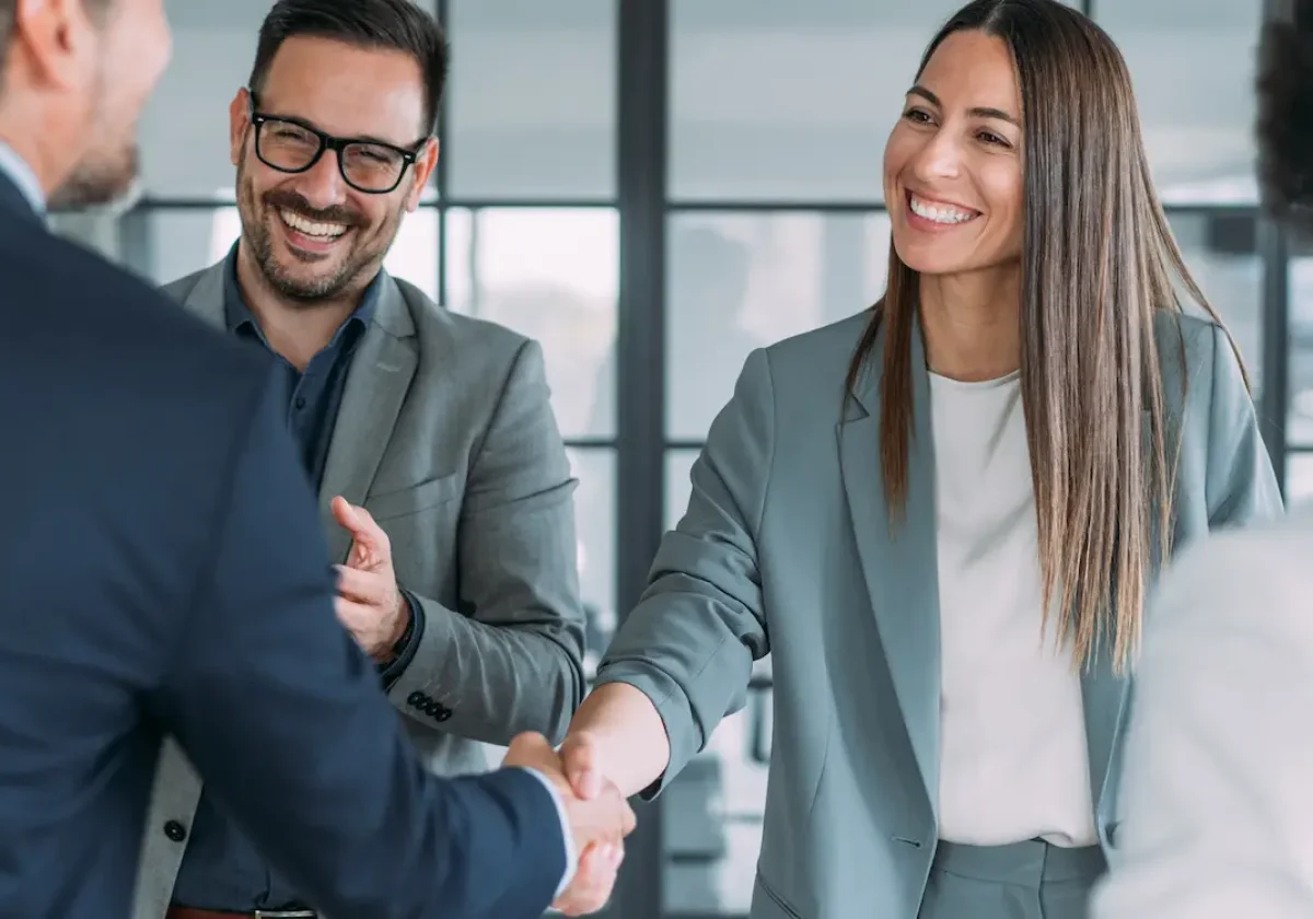 Geschäftsleute begrüßen sich mit einem Handschlag in einem modernen Büro mit Glasfront im Hintergrund