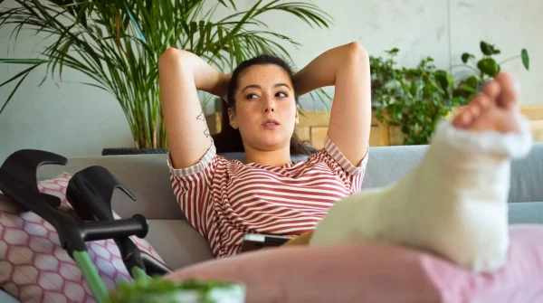 Junge Frau mit Gipsbein liegt auf dem Sofa, Krücken neben ihr – Symbolbild für Verletzung, Auszeit und Anspruch auf Genesungsgeld.